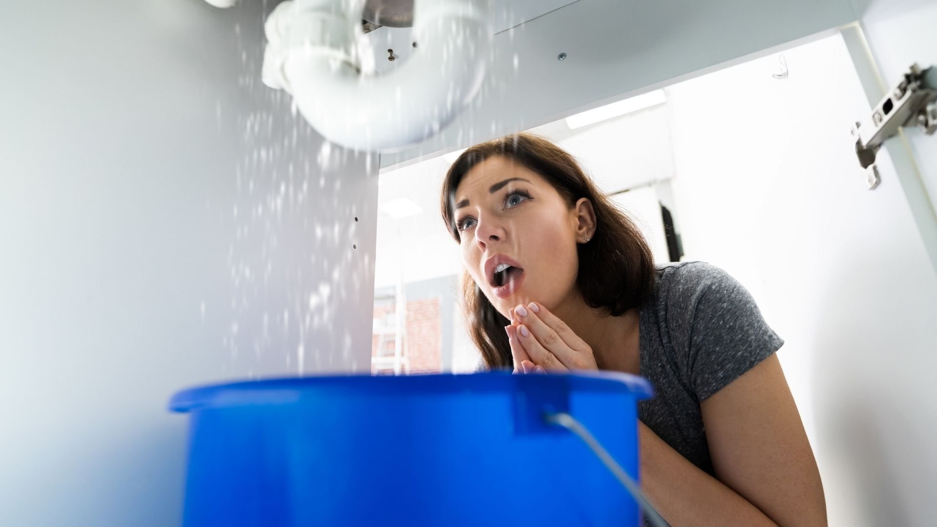 Woman looking shocked at water leaking from ceiling into blue bucket