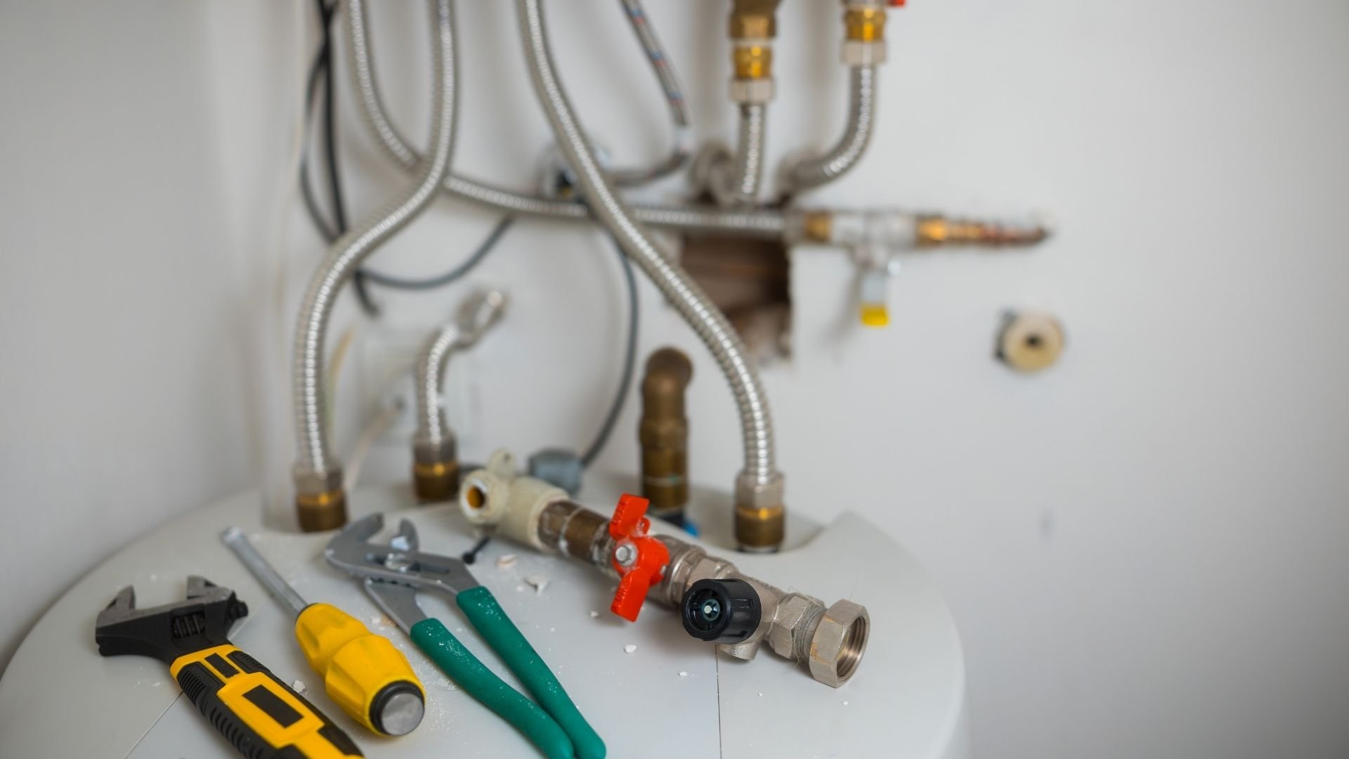 Plumbing tools and brass fittings arranged with metal flexible hoses and wall fixtures