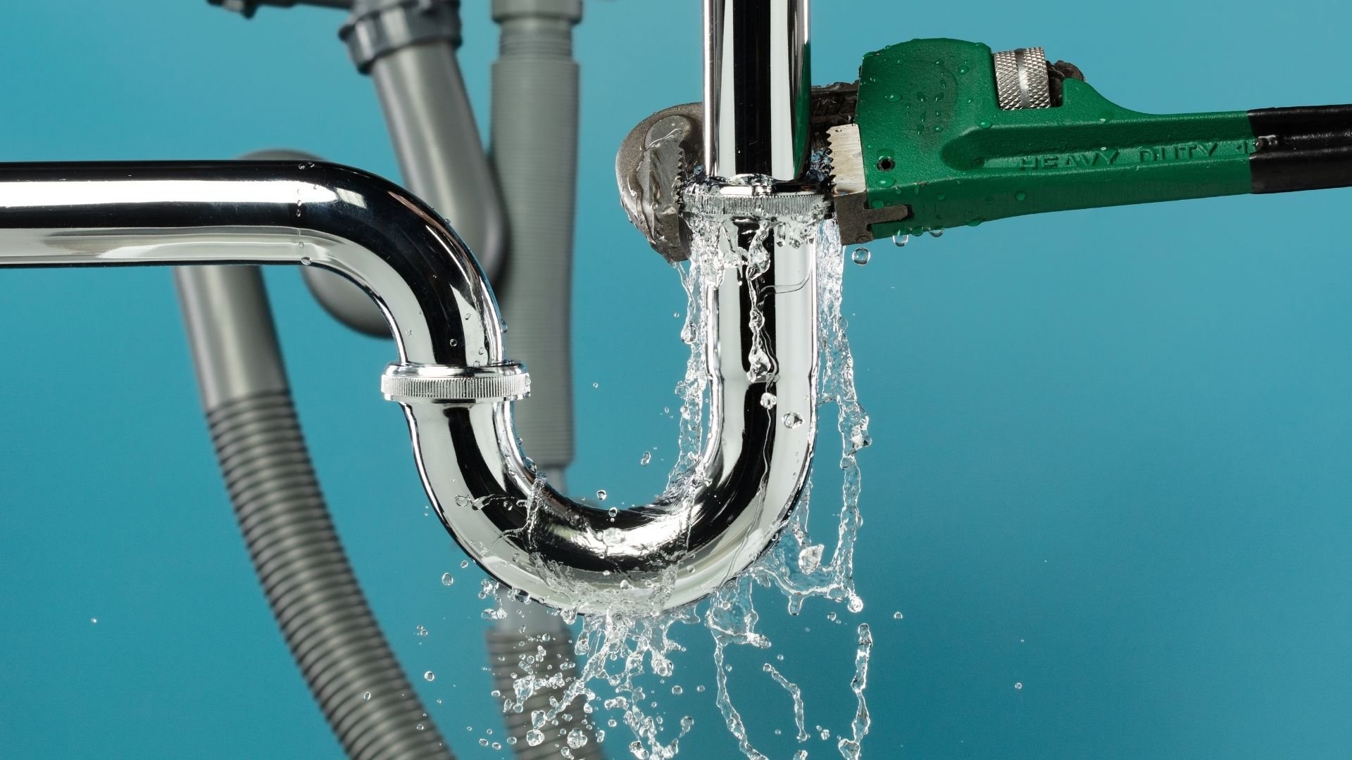 Water flowing from chrome pipes and green adjustable wrench against turquoise background