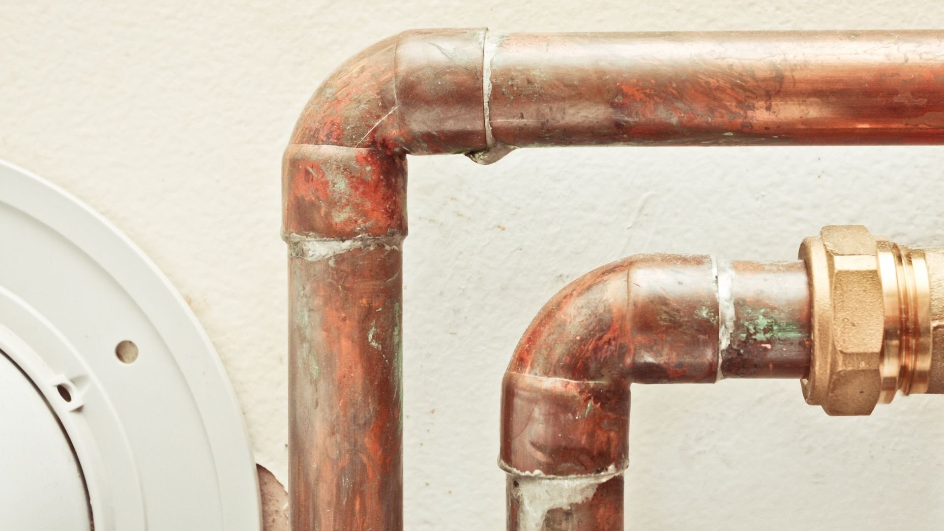 Old corroded copper pipes with elbow joint and brass fitting against white wall