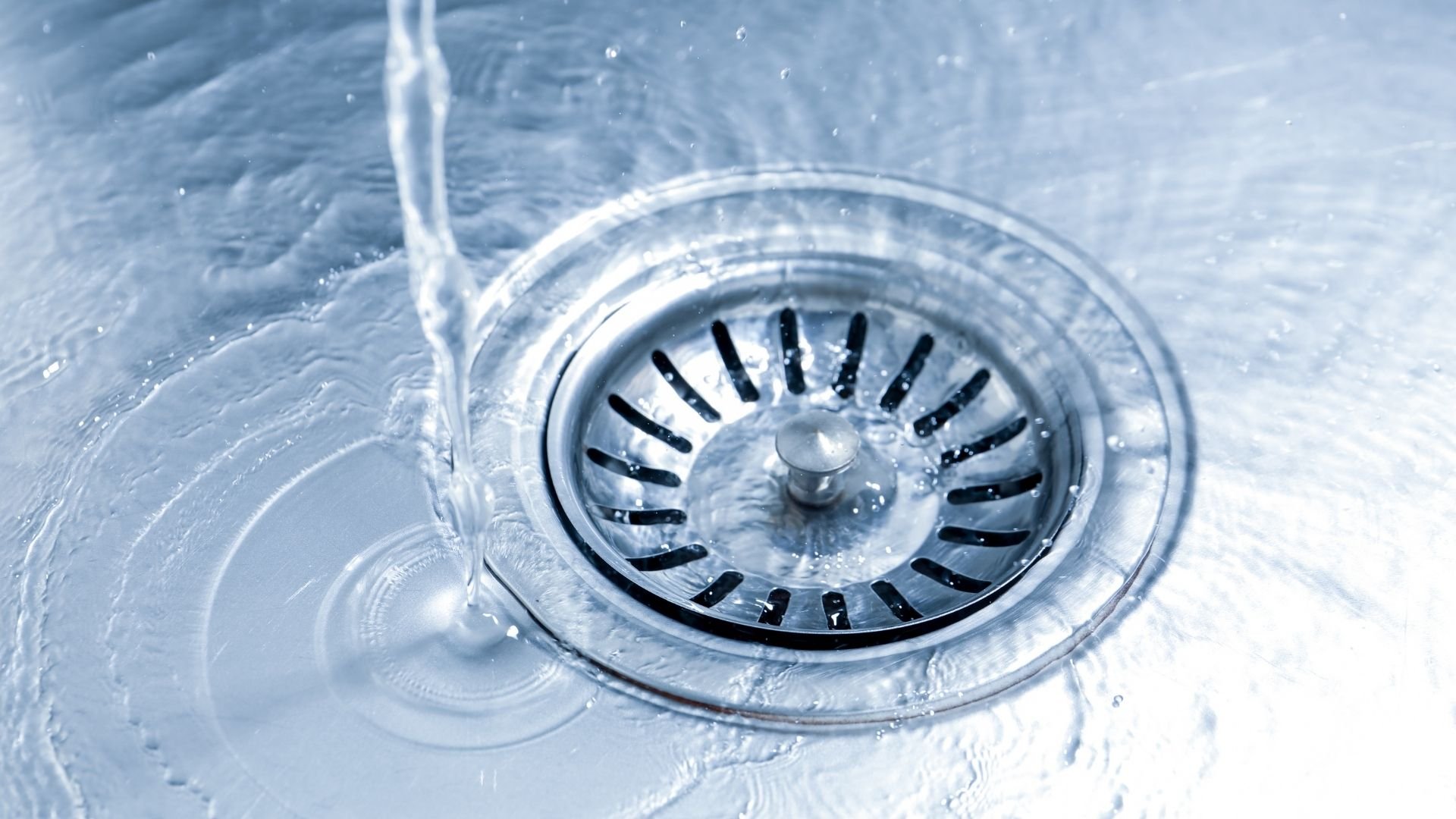 Water flowing into a kitchen sink drain with ripples and droplets visible