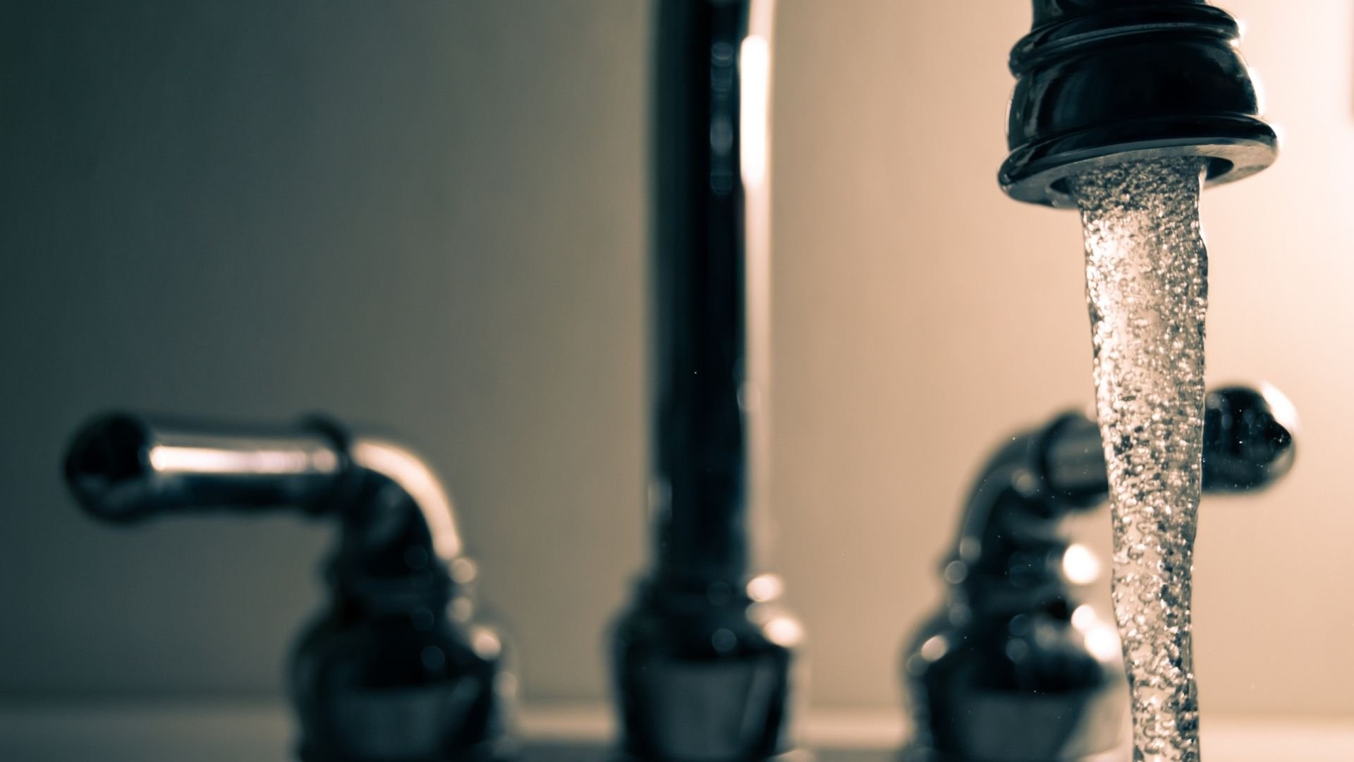 Water flowing from a corroded black faucet with blurred pipes in the background